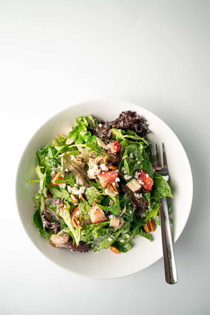Strawberry pecan summer salad in a white bowl with a fork