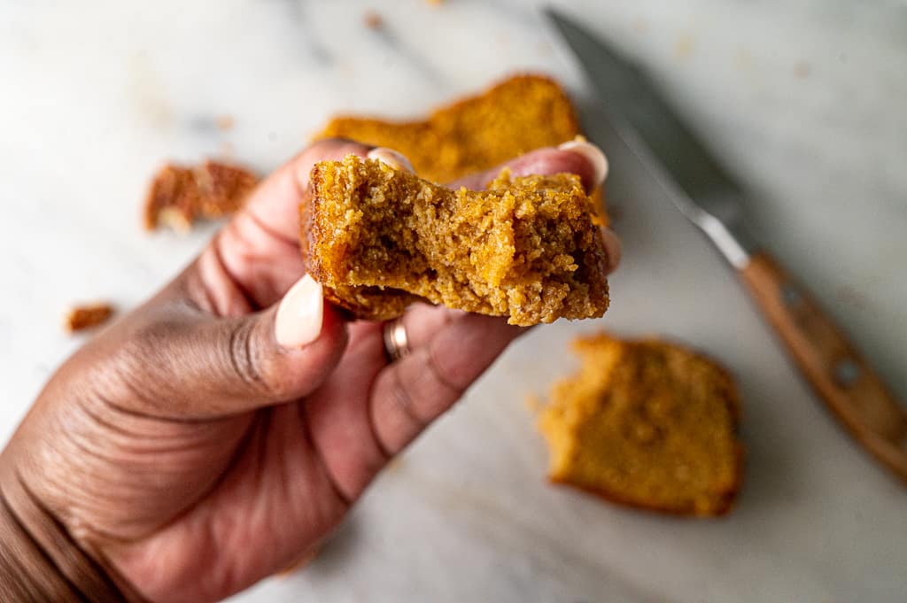 Piece of keto pumpkin bread held up to the camera with a knife and more bread in the background. 
