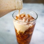 pumpkin pie coffee creamer poured into a tall glass of iced coffee