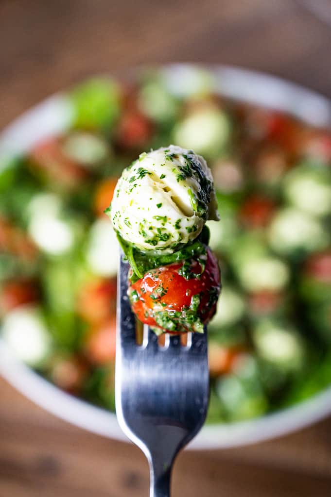 Mozzarella basil and tomato covered in chimichurri on a fork above kale caprese salad