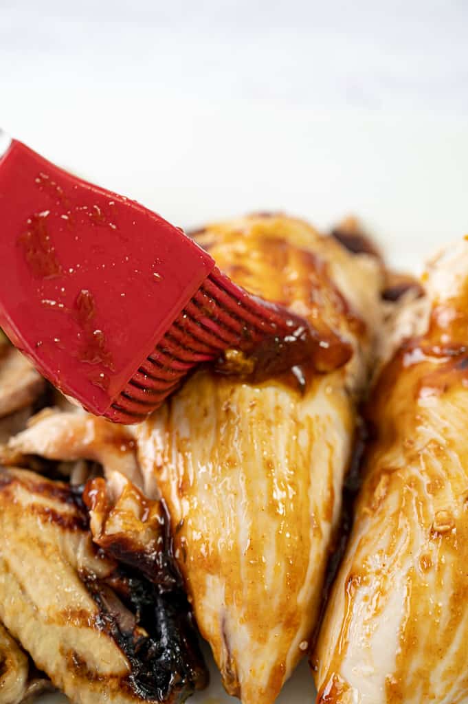 Brushing pressure cooker chicken with a red rubber brush. 