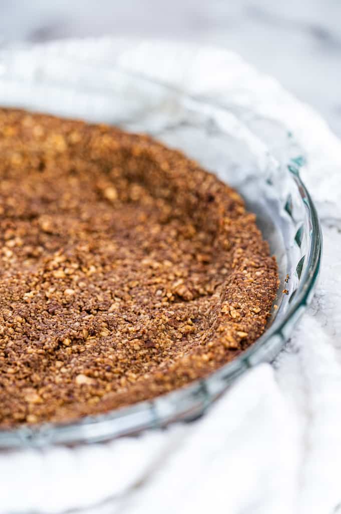 Nut pie crust in a pie dish with a towel around it