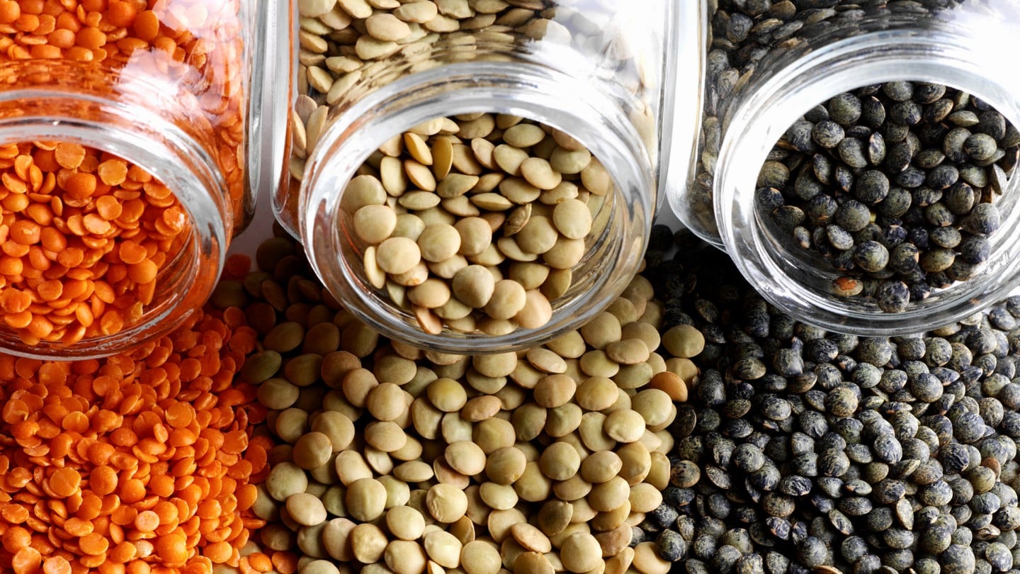 red, green and black lentils poured out of a glass jar. 