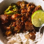 Beef and broccoli in a bowl with a lime and rice