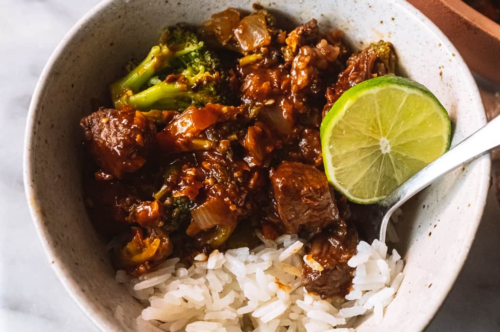 Beef and broccoli in a bowl with a lime and rice