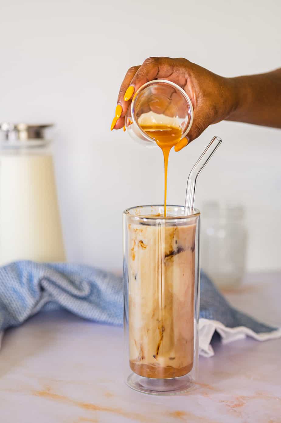 Frozen coffee ice cubes in tall double walled glass with a straw with caramel poured over.