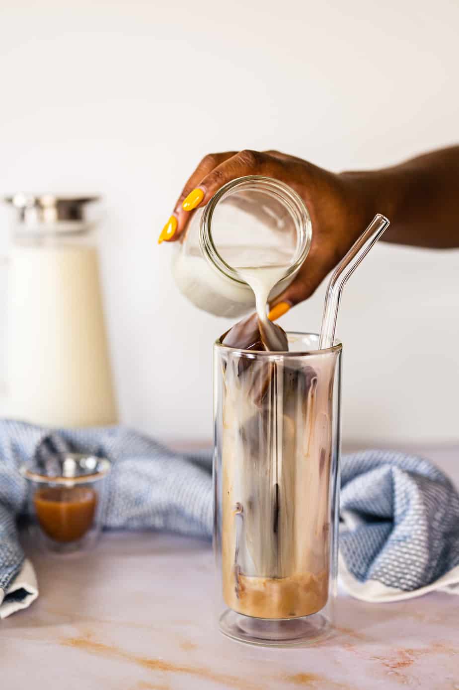 Frozen coffee ice cubes in tall double walled glass with a straw with milk poured over ice cubes.