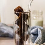 Frozen coffee ice cubes in tall double walled glass with a straw.