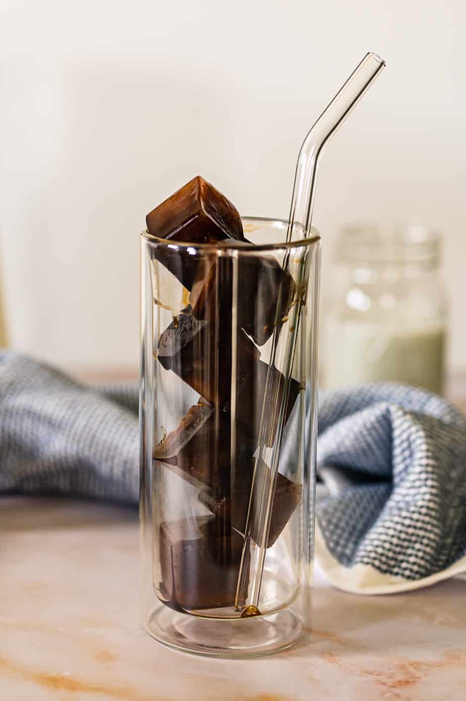 Frozen coffee ice cubes in tall double walled glass with a straw.