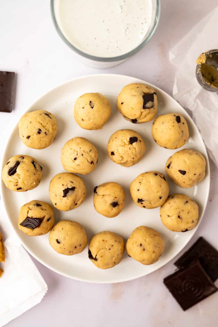 edible chocolate chip cookie dough balls with milk, a cookie scoop and chocolate.