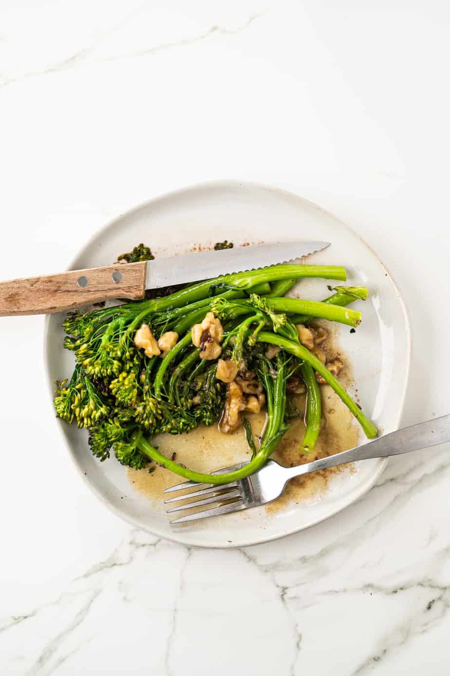broccolini on a plate on marble with walnuts and vinaigrette 
