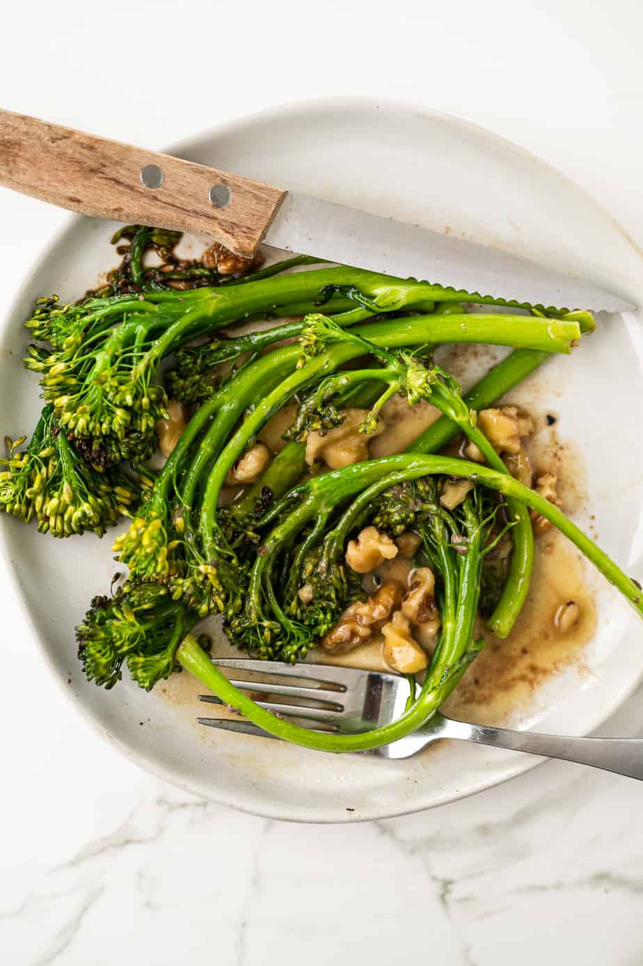 Above shot of broccolini on a plate on marble with walnuts 