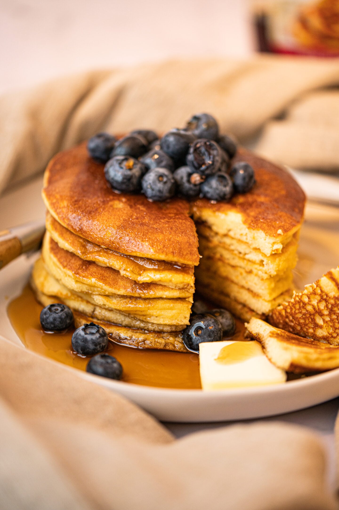 Vertical image, Golden almond‑flour pancakes stacked tall, covered in syrup and fresh blueberries, styled in a cozy kitchen setting