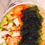 shot from above of TikTok Salmon Bowl with nori, avocado, mayo, salmon and an avocado in frame for decor.