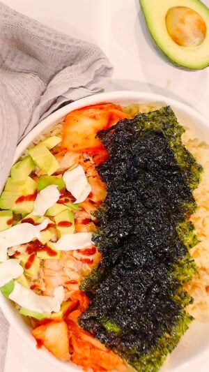 shot from above of TikTok Salmon Bowl with nori, avocado, mayo, salmon and an avocado in frame for decor.