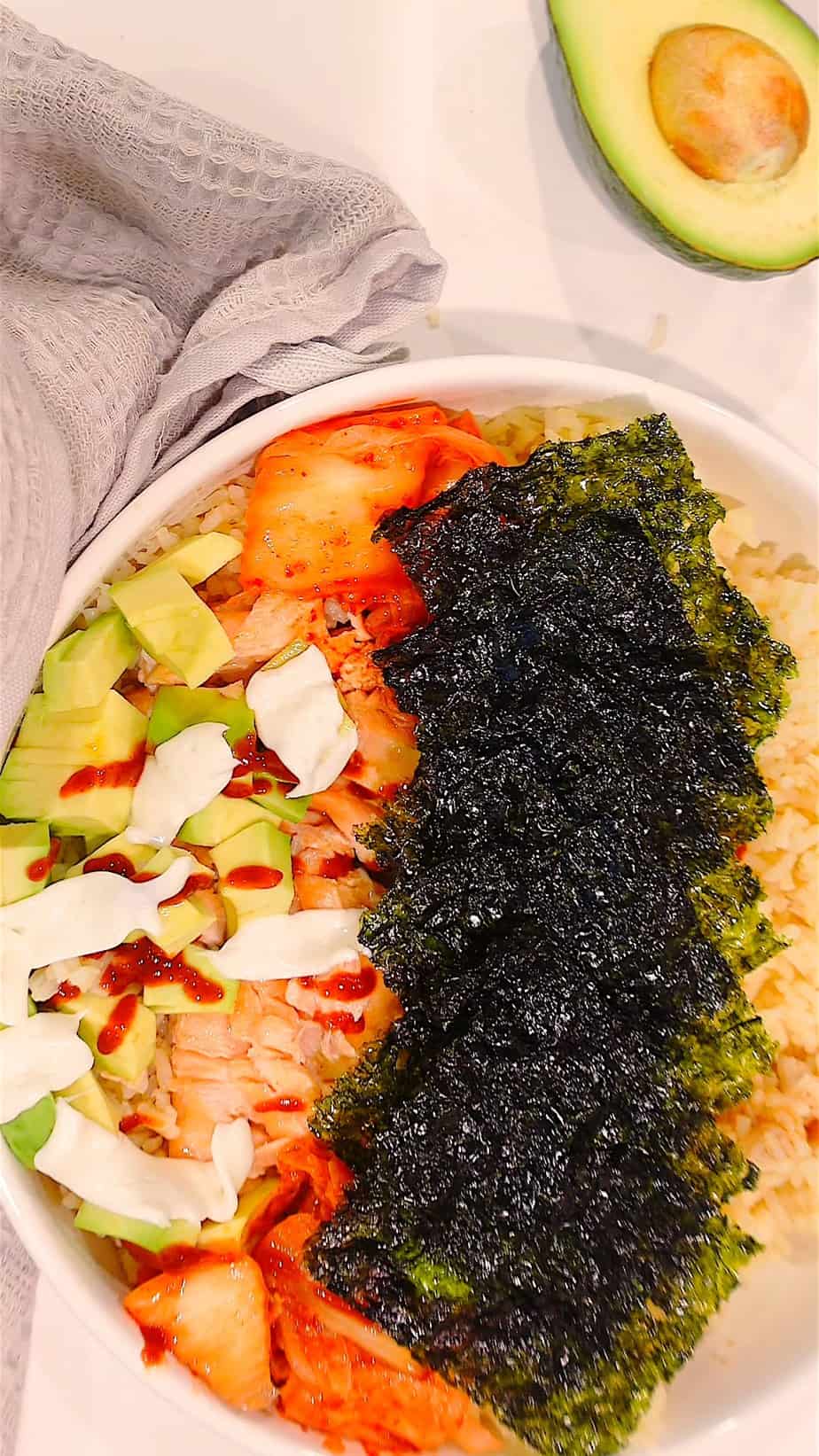 shot from above of TikTok Salmon Bowl with nori, avocado, mayo, salmon and an avocado in frame for decor.