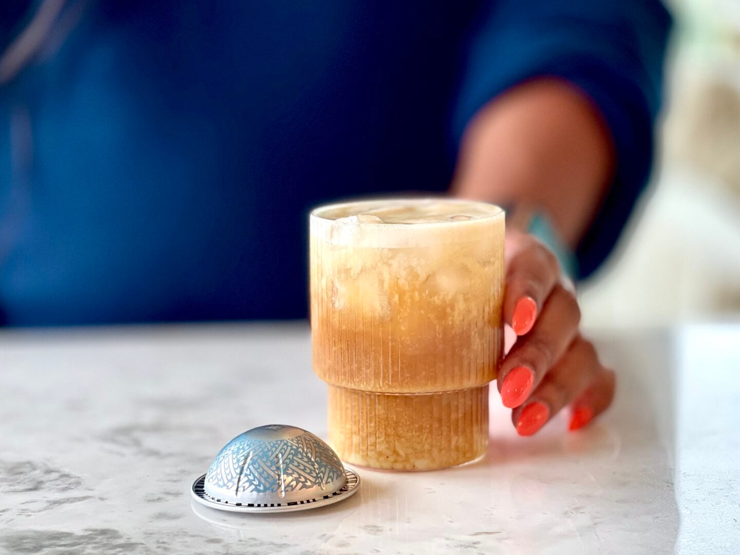 pistachio latte with oat milk and hand touching it with a nespresso kona pod