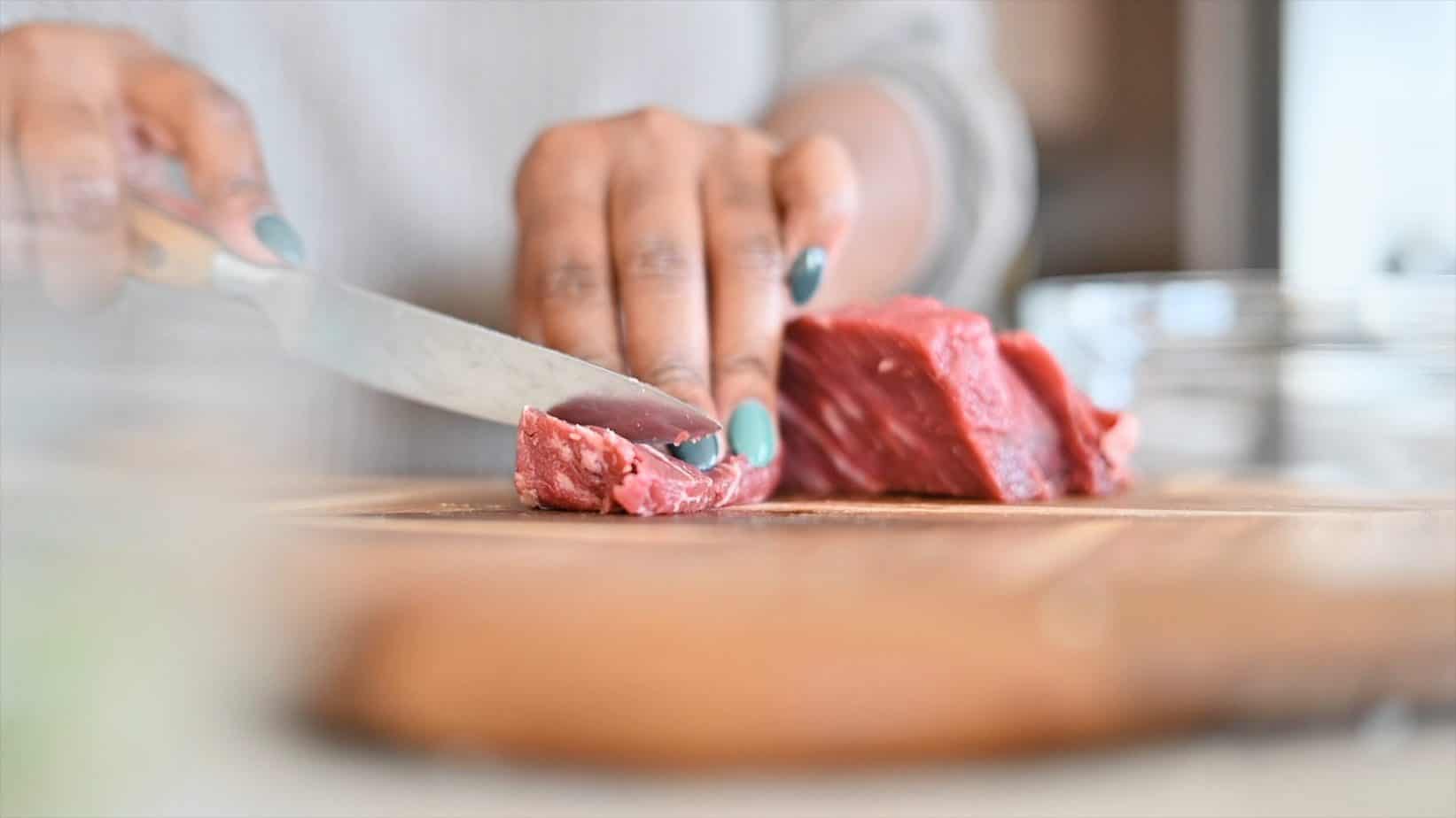 Mila chopping steak on a wooden cutting board
