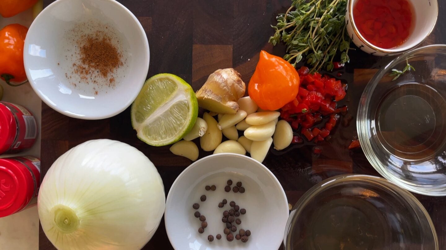 Some ingredients for jamaican jerk marinade laid out on a wooden cutting board.
