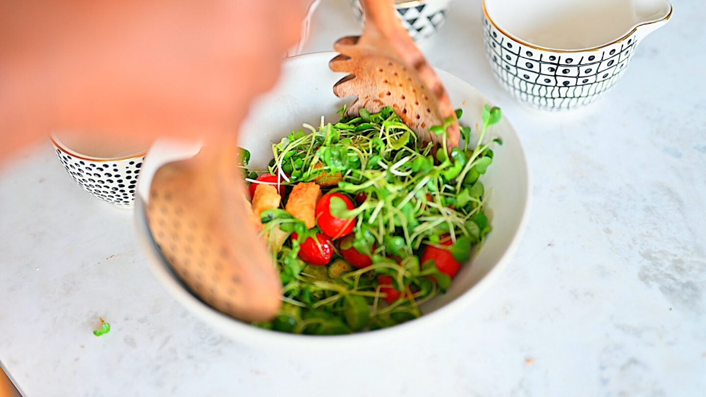 Microgreens salad being tossed to coat in dressing