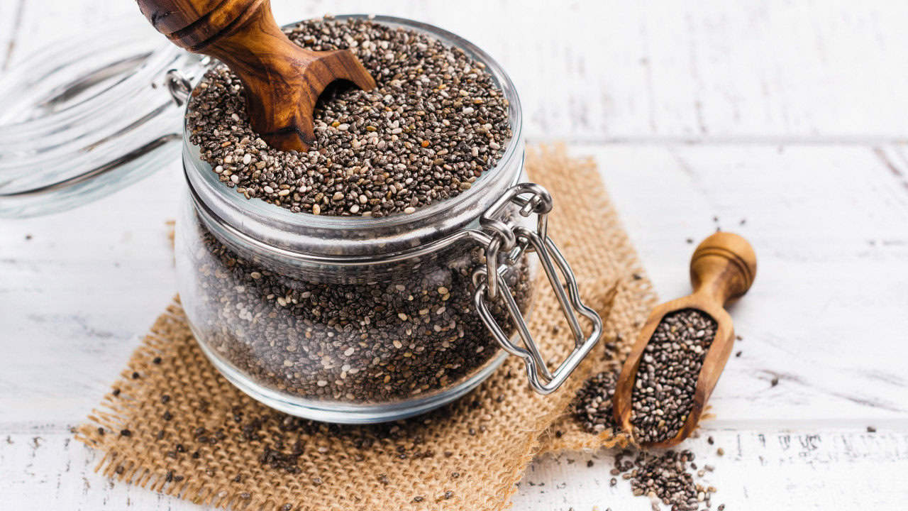 Chia seeds in a mason jar cannister with a scoop filled with chia seeds to the side.