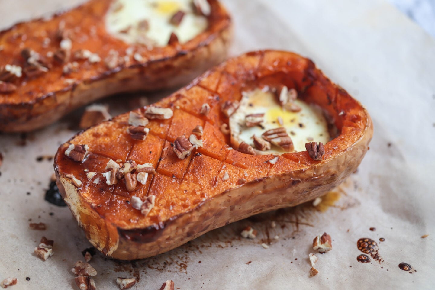 butternut squash on parchment paper with an egg where the scooped seeds would be and pecans sprinkled on top.