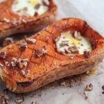 butternut squash on parchment paper with an egg where the scooped seeds would be and pecans sprinkled on top.