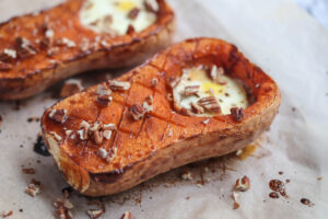 butternut squash on parchment paper with an egg where the scooped seeds would be and pecans sprinkled on top.