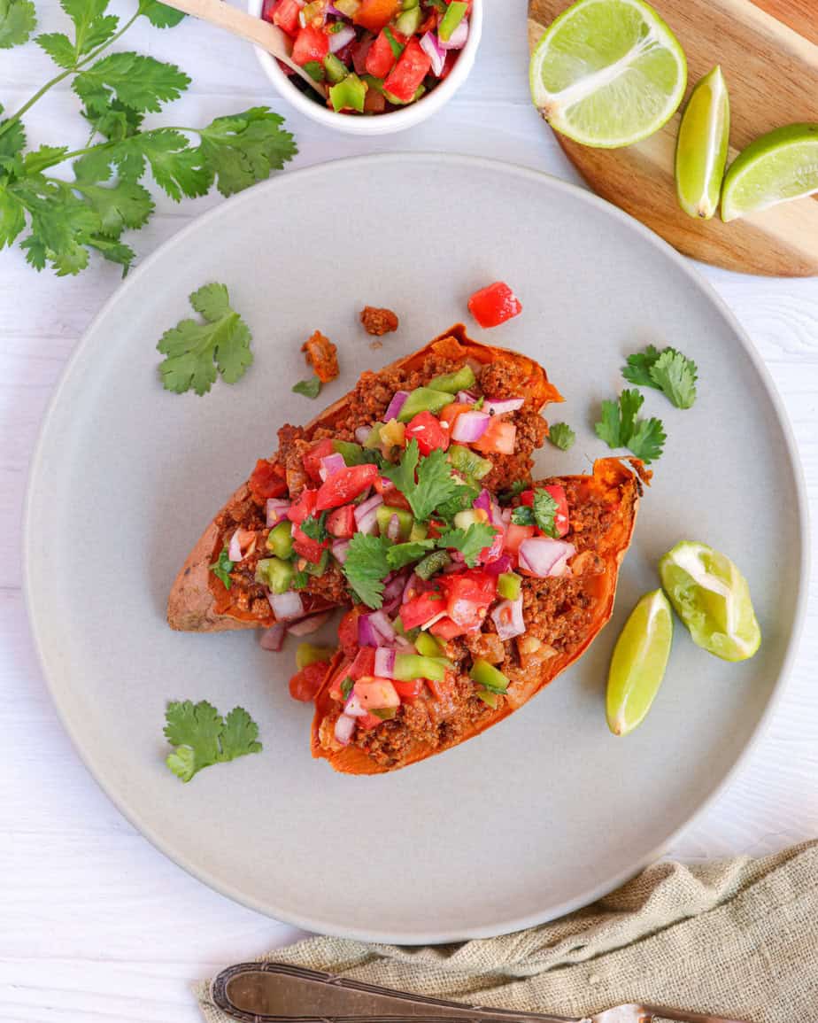 Top-down shot of sweet potato taco boats with vibrant tomato salsa and cilantro, plated with lime wedges on a light wooden table