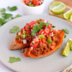 Side angle of sweet potato taco boats filled with seasoned beef and colorful salsa, served with fresh cilantro and lime slices