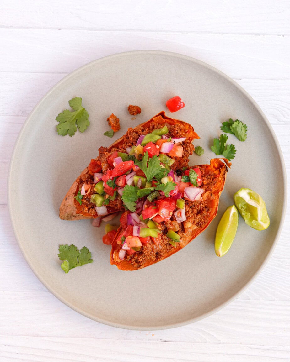 Overhead view of sweet potato taco boats topped with ground beef and fresh salsa, garnished with cilantro and lime wedges on a gray plate"